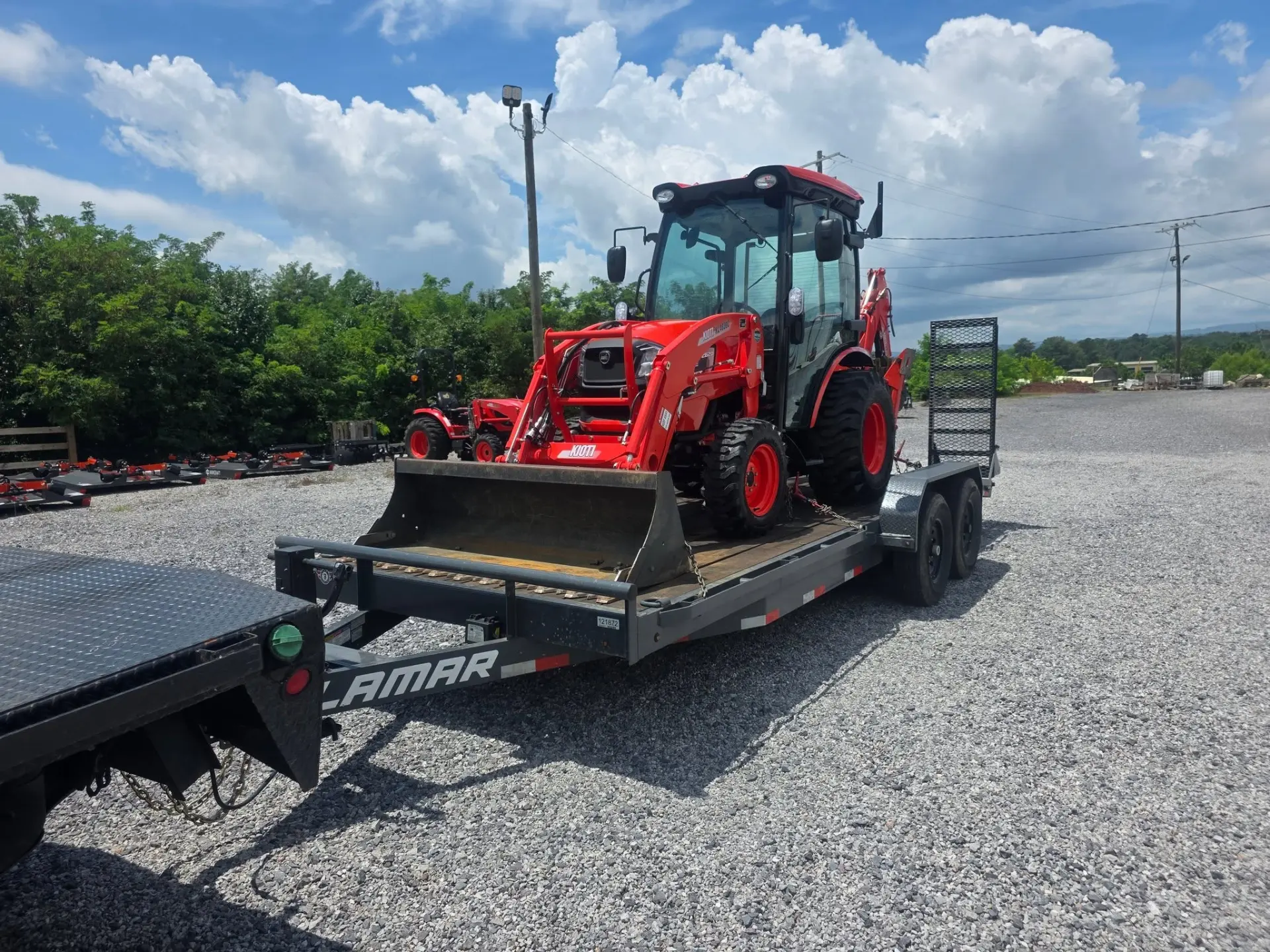 Compact tractor with front loader and backhoe loaded on an equipment trailer