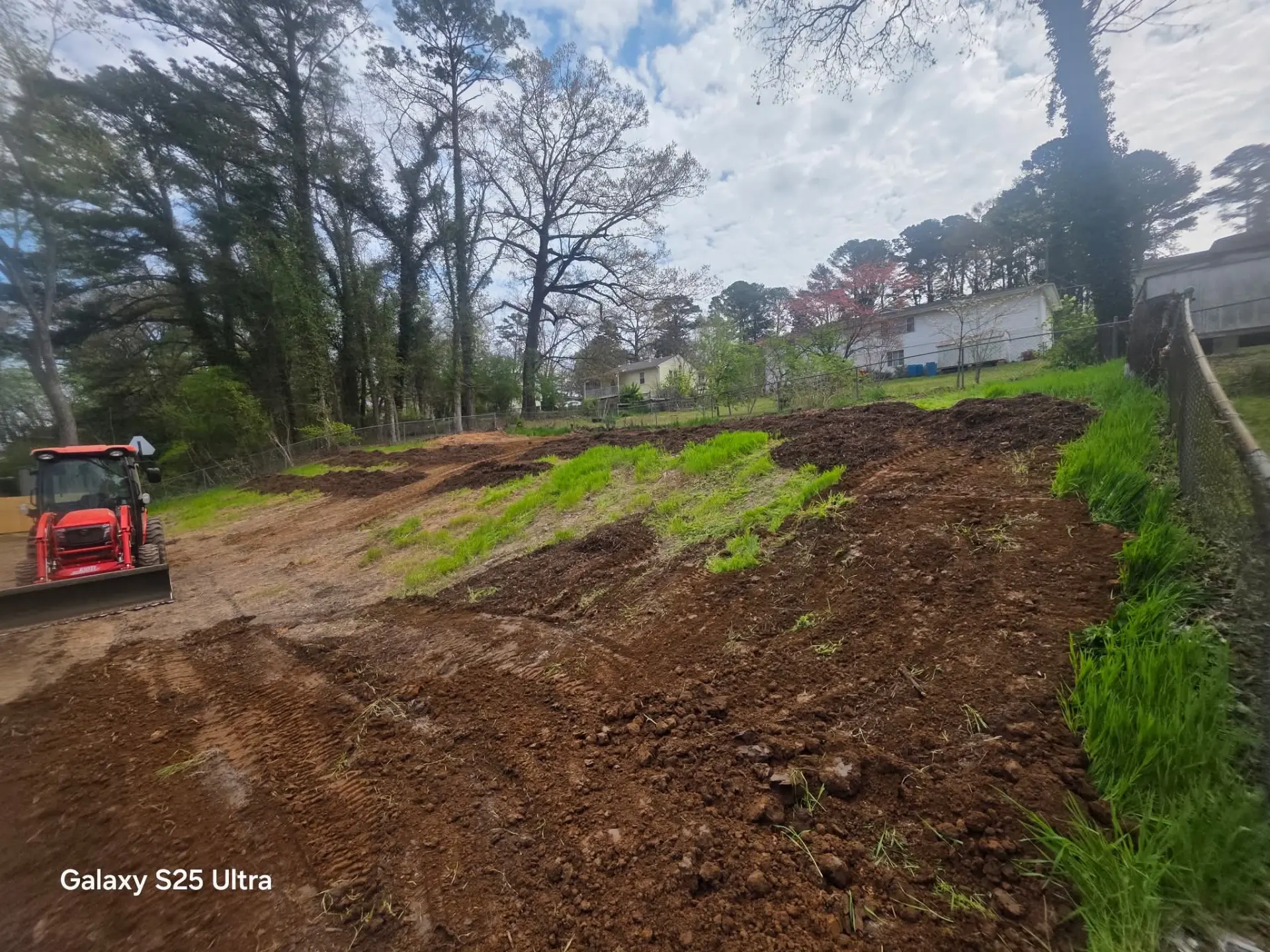 Sloped yard regraded with fresh dirt beside a red tractor with loader
