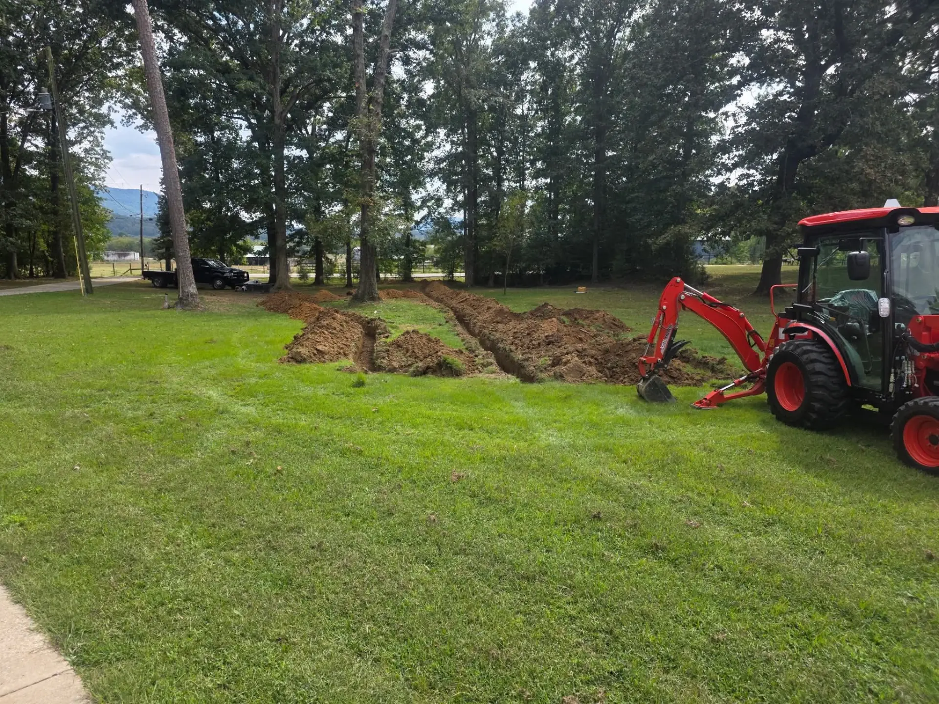 Parallel trenches dug across a lawn with a backhoe next to them