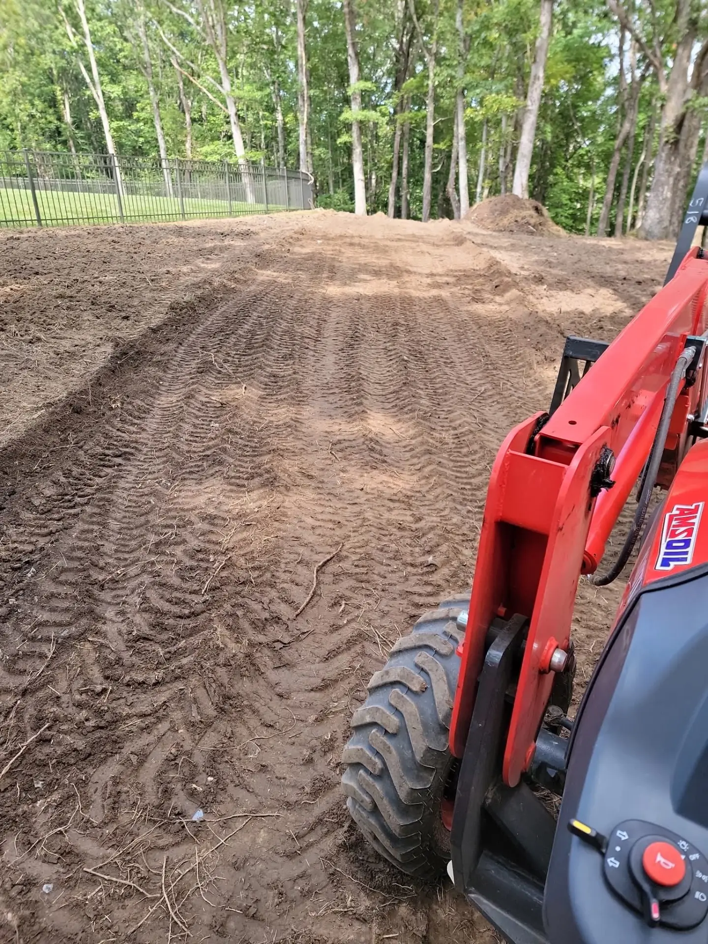 Freshly graded dirt yard beside a tractor loader near a fence