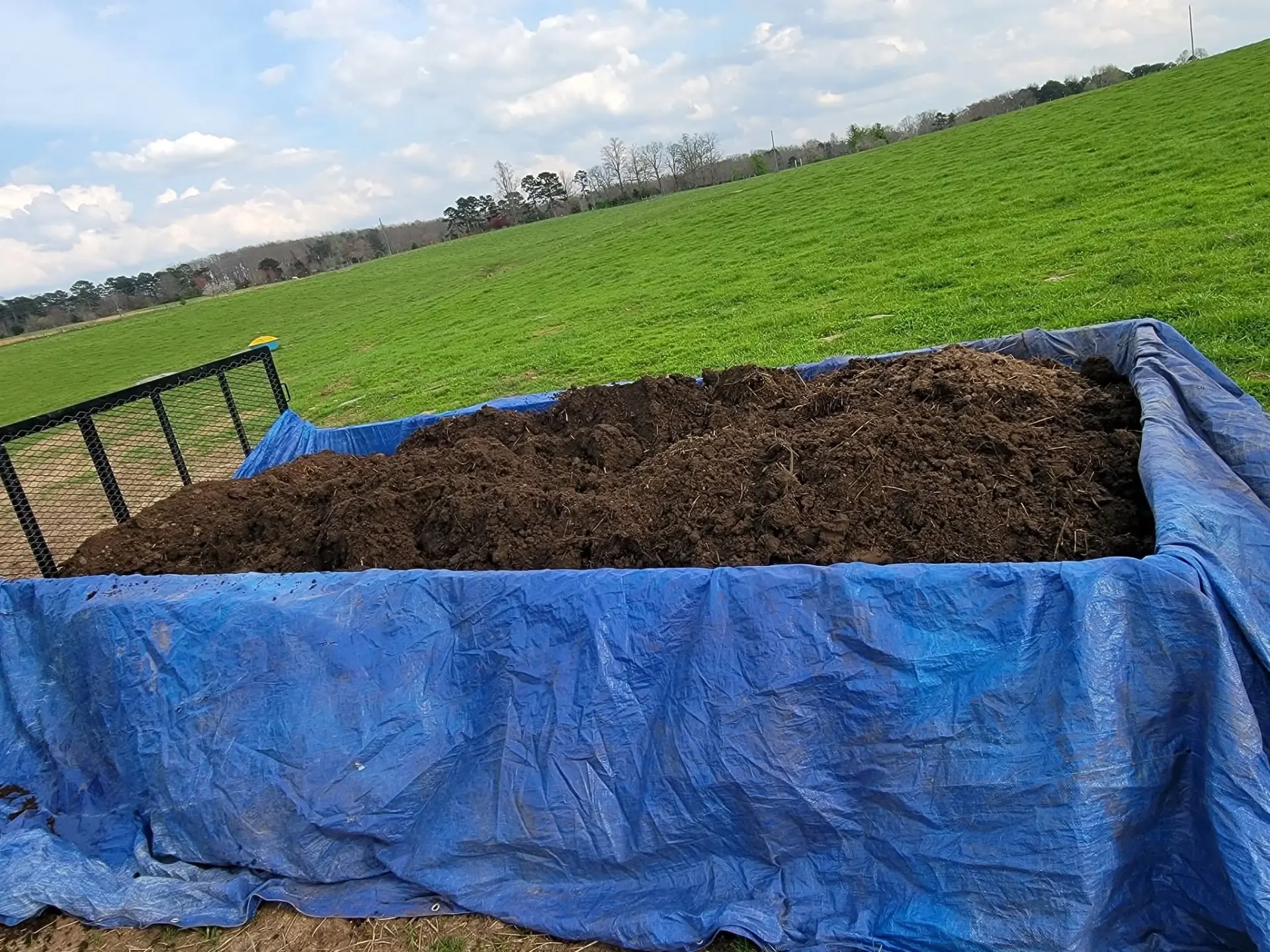 Trailer loaded with dark topsoil in a green field