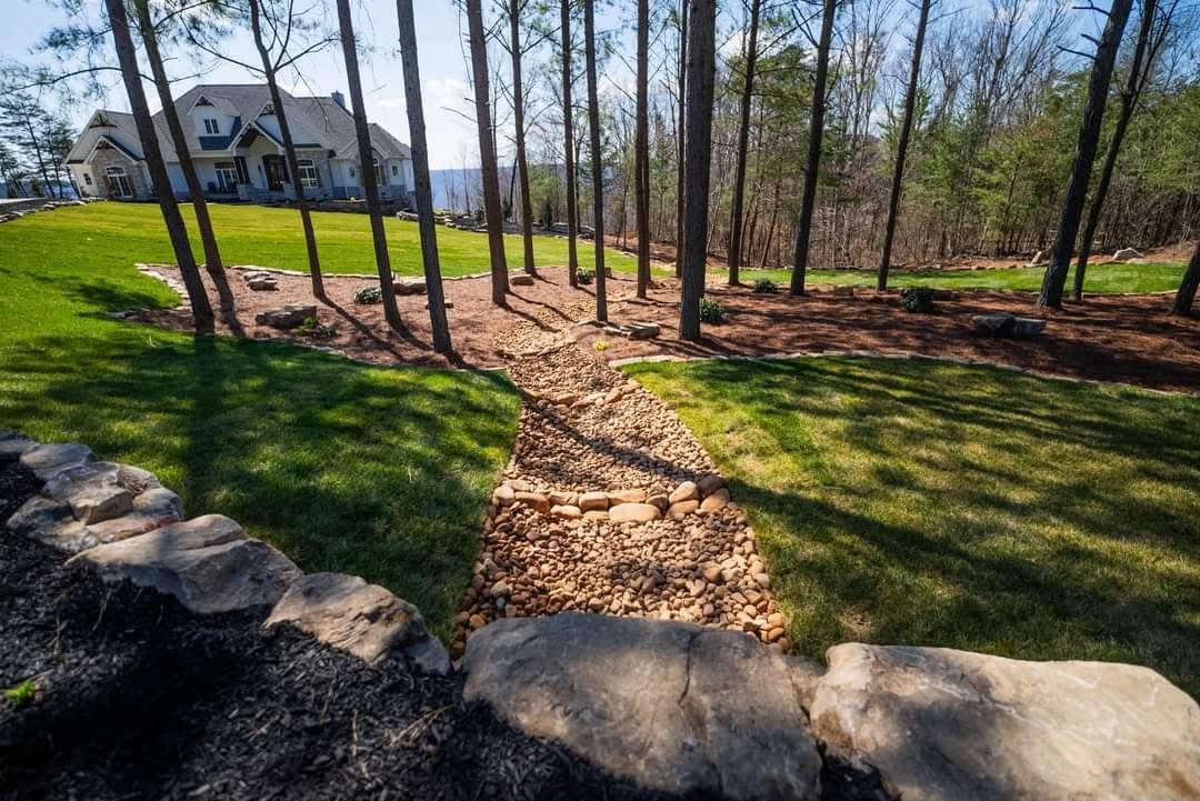 River rock drainage path between green lawns below a mountain home