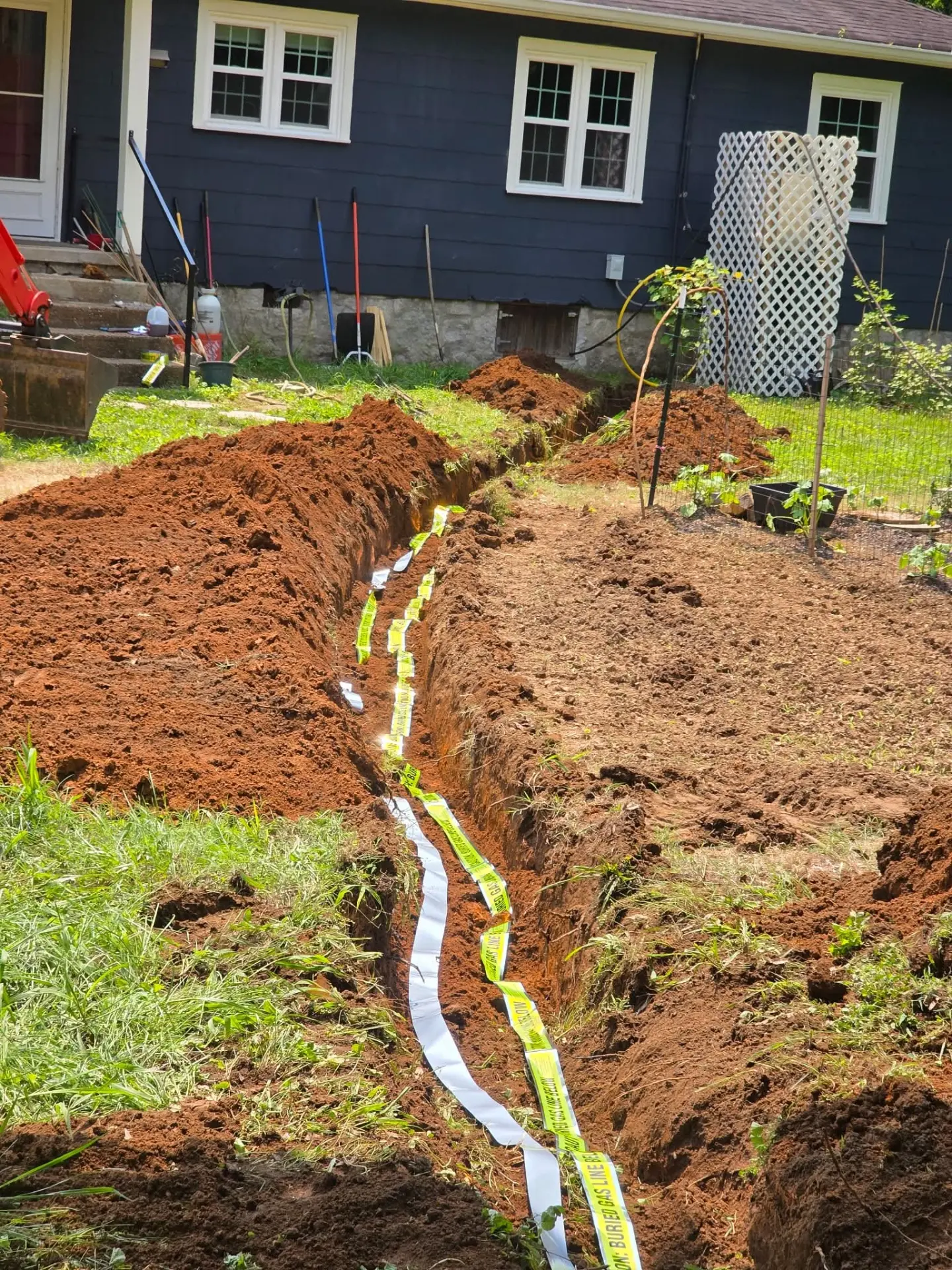 Trench dug across a backyard for a buried gas line with warning tape