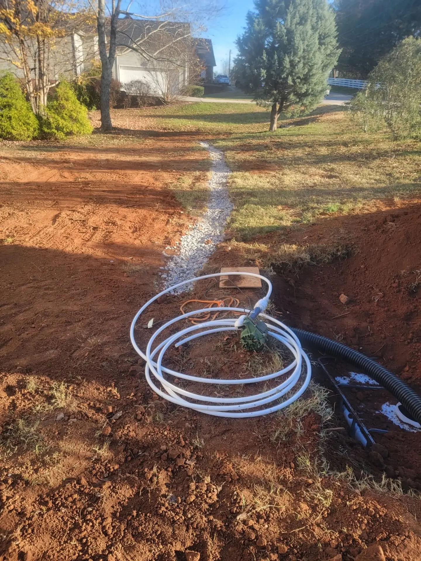 Gravel drainage channel with sump pump line and corrugated pipe in a yard
