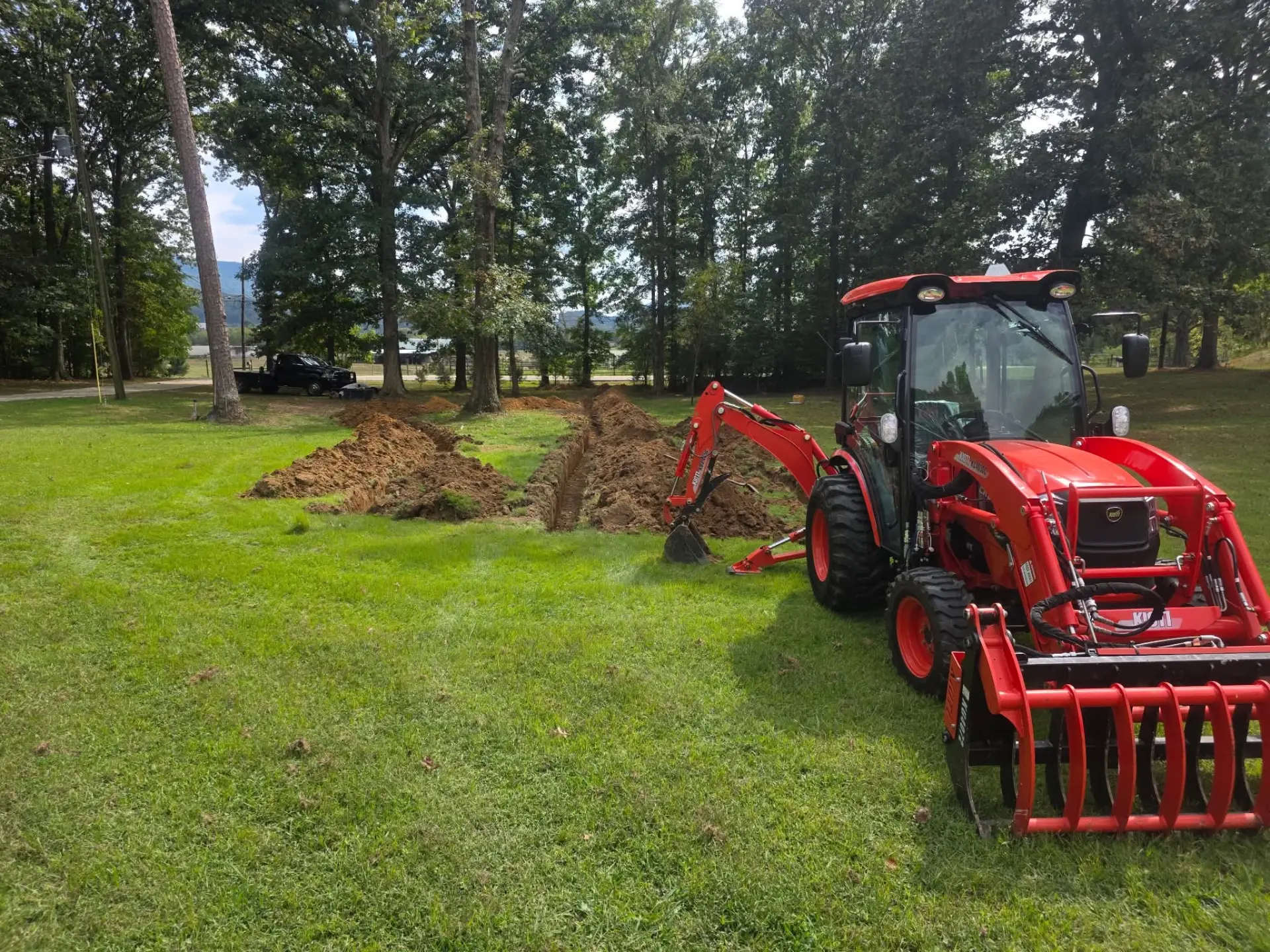 Red tractor loader backhoe beside freshly dug trenches in a grassy lot
