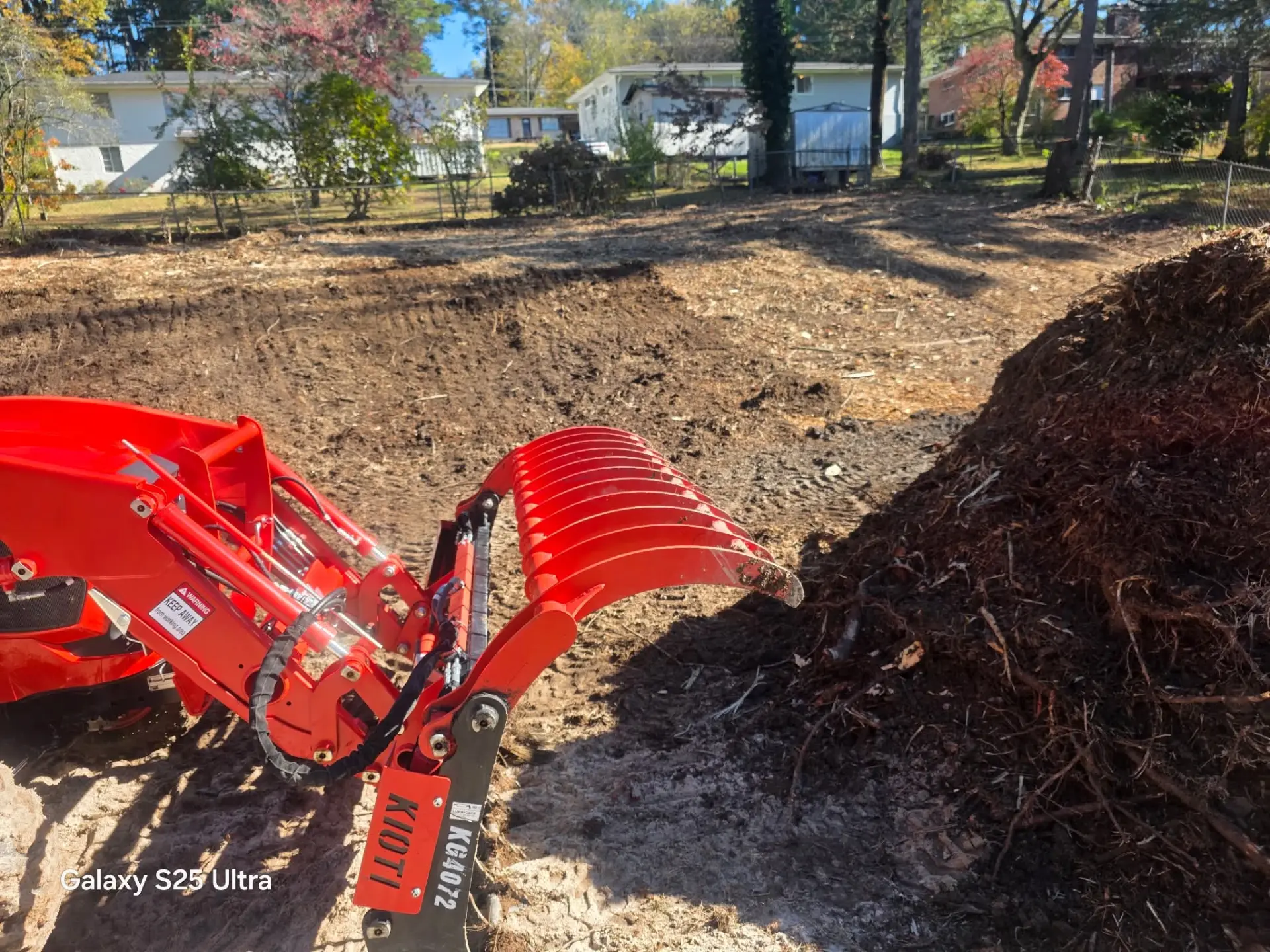 Root rake grapple on a red tractor next to a pile of cleared roots and debris