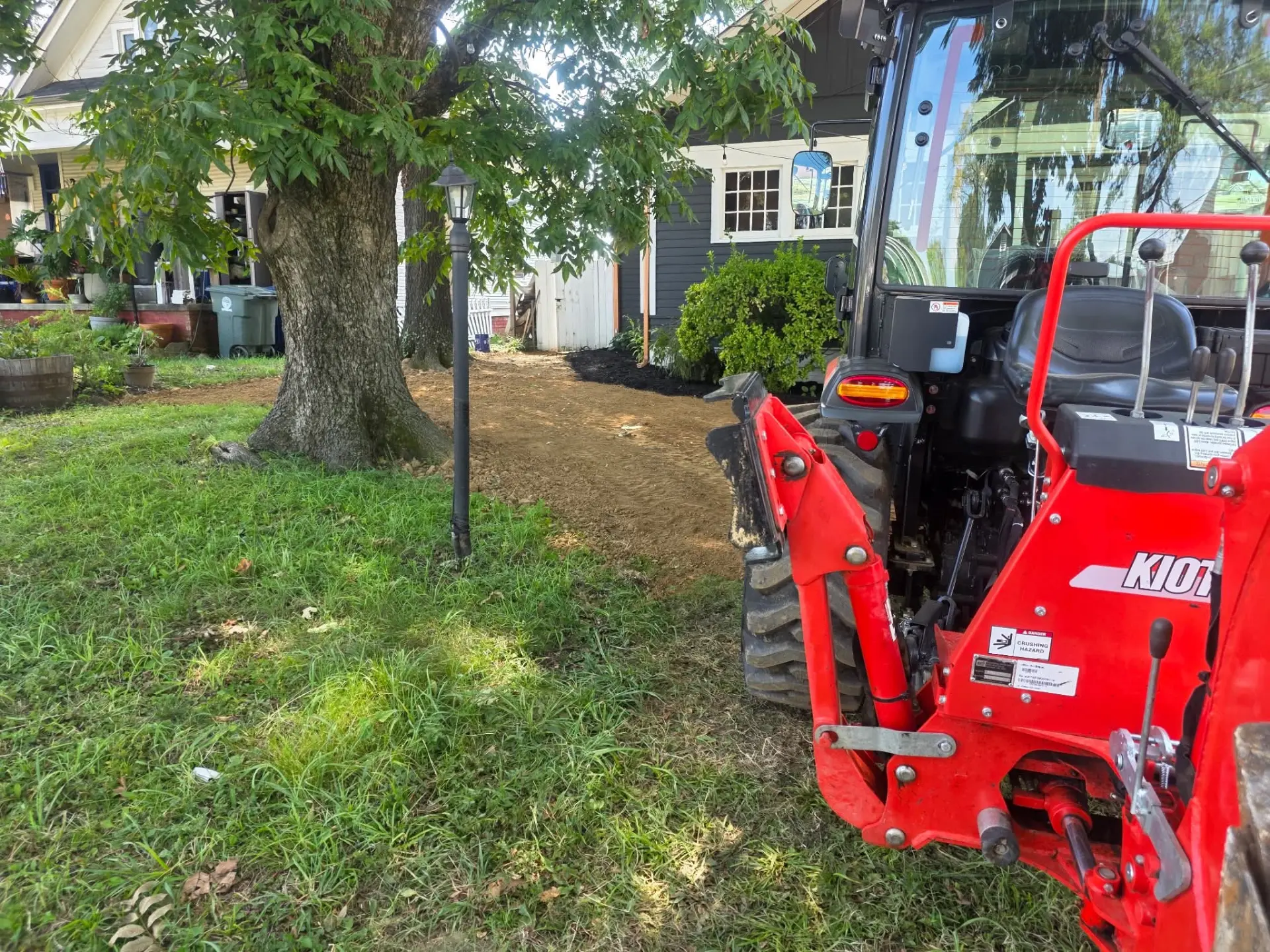 Graded dirt path beside a tree next to a tractor in a front yard