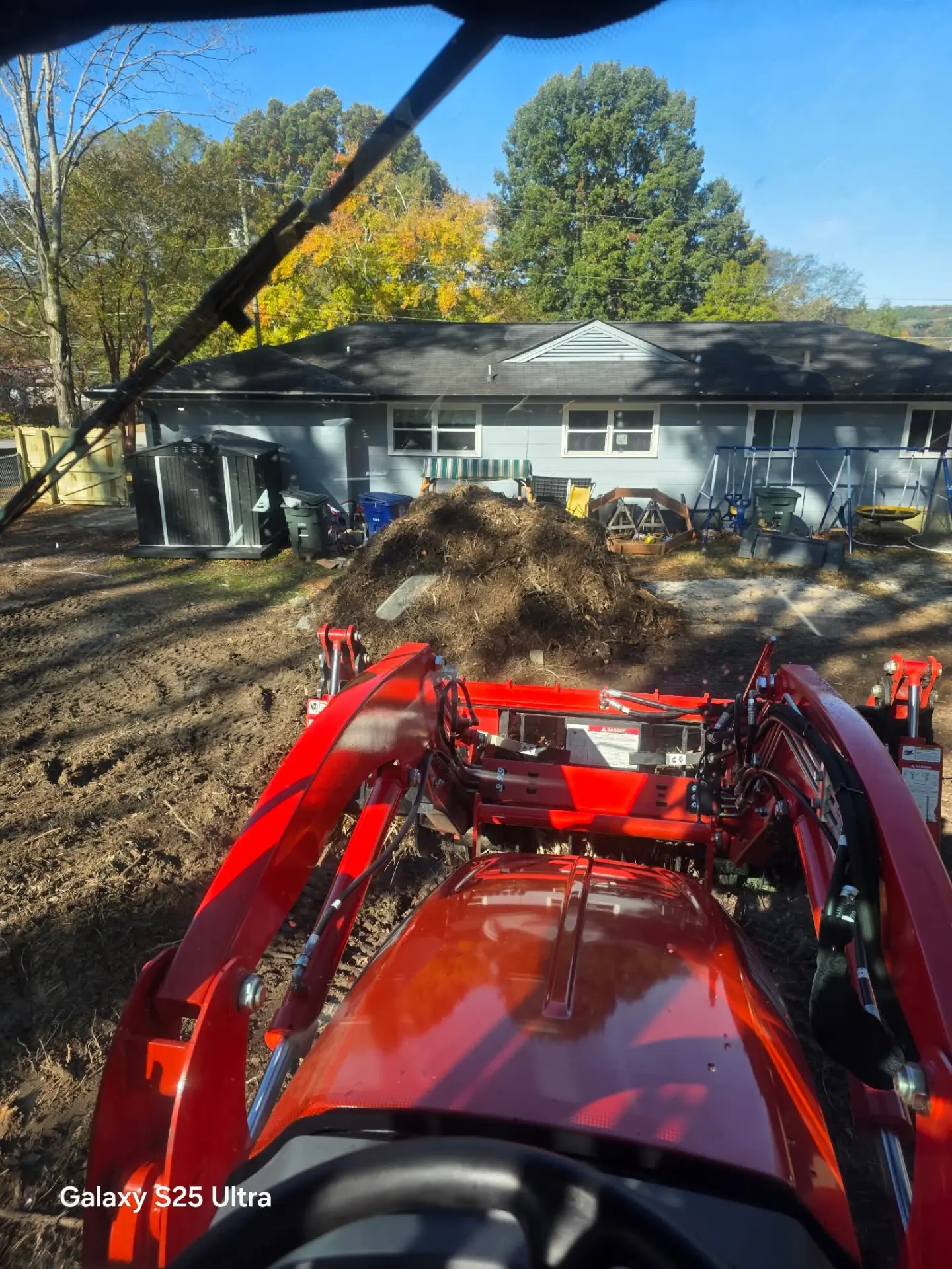 Tractor loader pushing a large pile of cleared brush and roots in a backyard