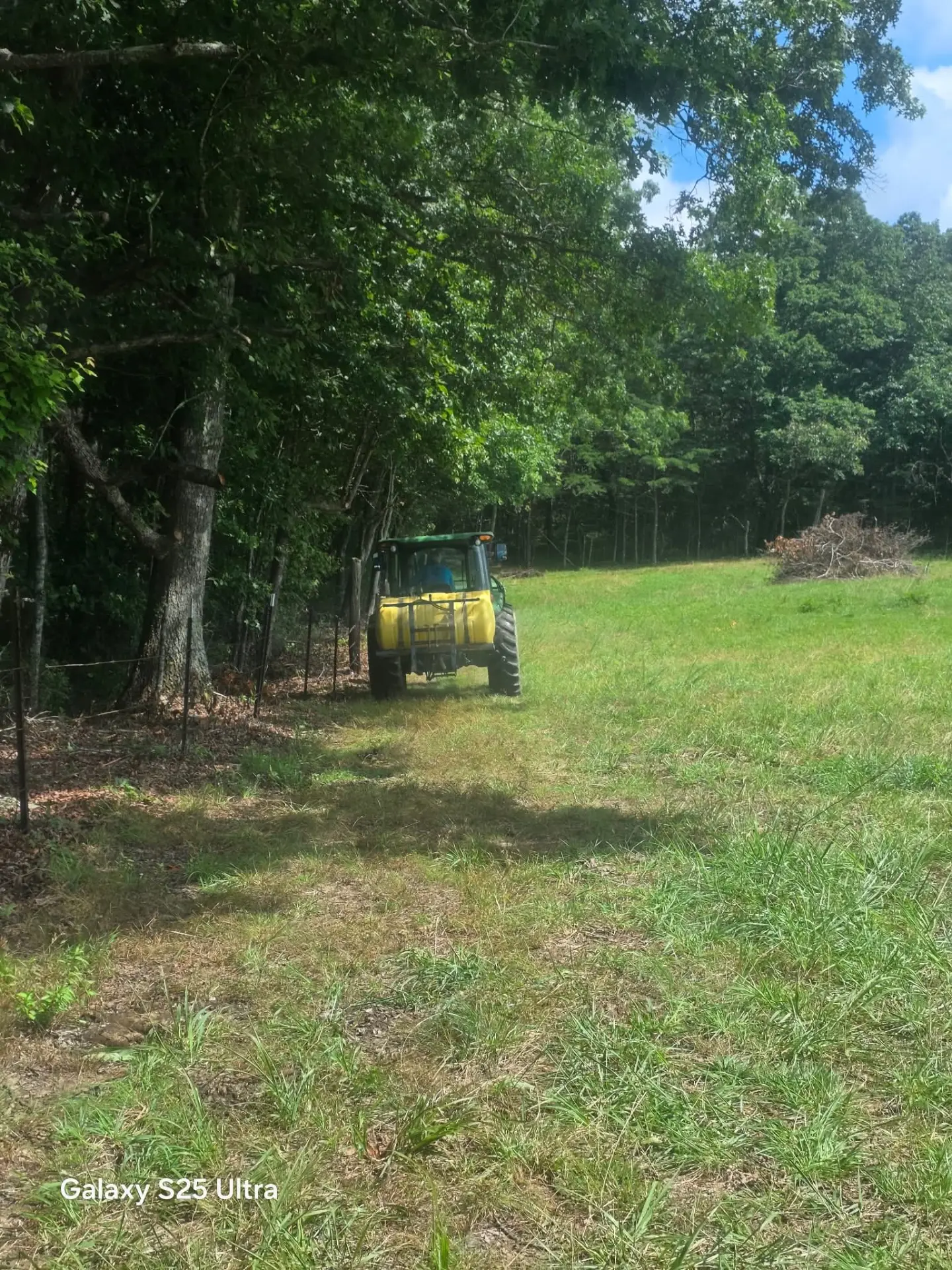 Tractor bush hogging a large grassy field next to the tree line