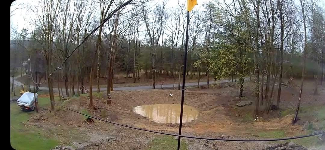 Newly excavated pond basin holding water in a wooded lot