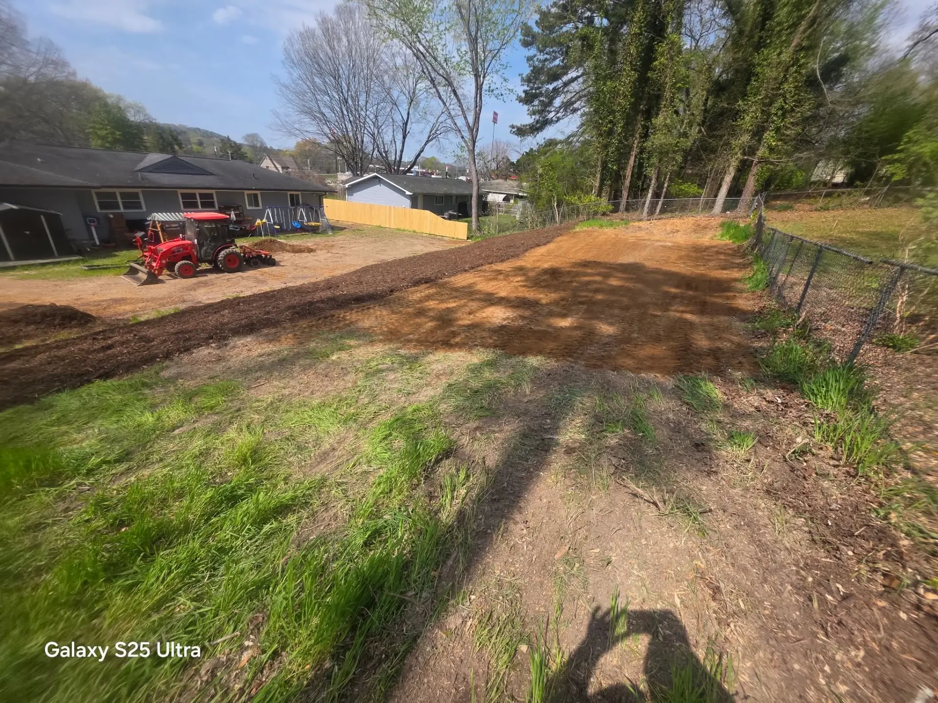 Backyard cleared and graded with fresh topsoil and a red tractor in the background