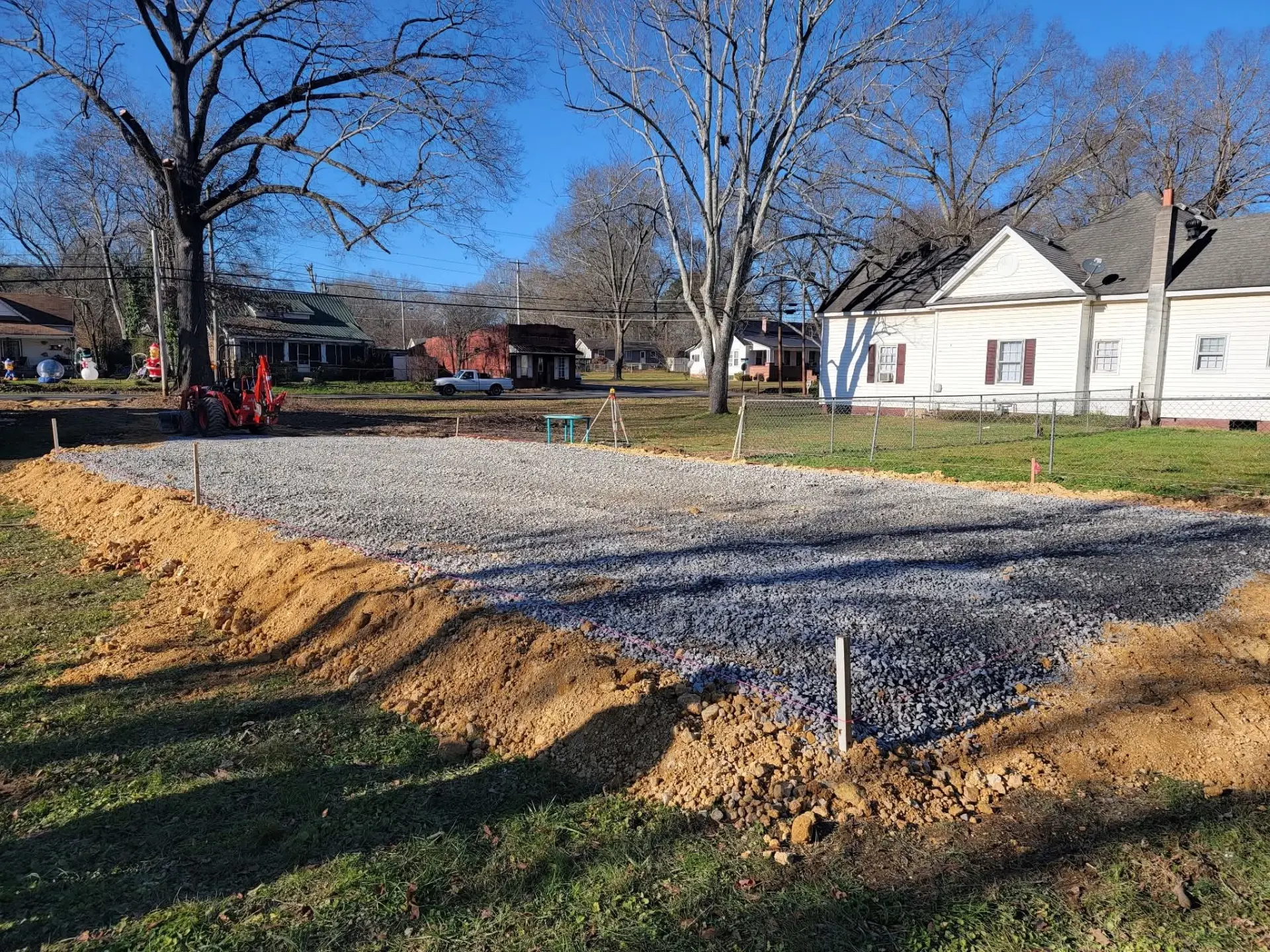 Gravel building pad staked out with a tractor backhoe nearby