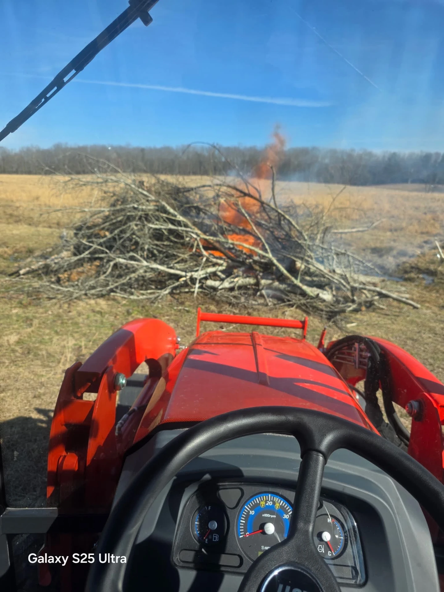 Brush pile burning in an open field seen from the tractor cab